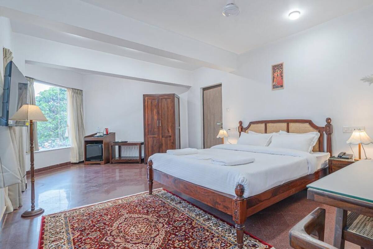 A bedroom with a wooden bed, bedside lamps, a desk, and a large window.