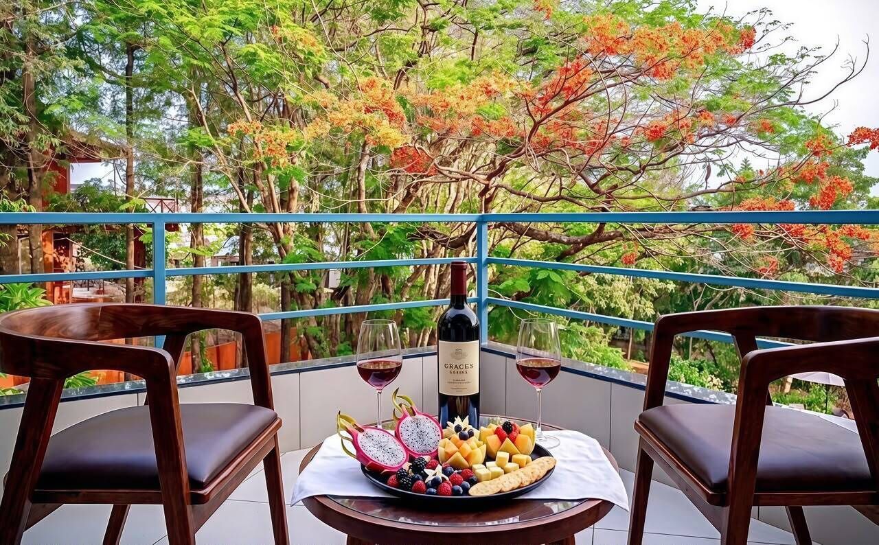 Uma varanda com duas cadeiras de madeira, uma mesa com uma garrafa de vinho, copos e uma travessa de frutas.