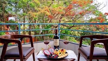 Uma varanda com duas cadeiras de madeira, uma mesa com uma garrafa de vinho, copos e uma travessa de frutas.