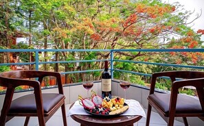 A balcony with two wooden chairs, a table with a bottle of wine, glasses, and a fruit platter. - Table Land Retreat (Mahabaleshwar)