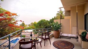 A balcony with a dining table, chairs, a hanging swing, and a view of trees and a body of water.