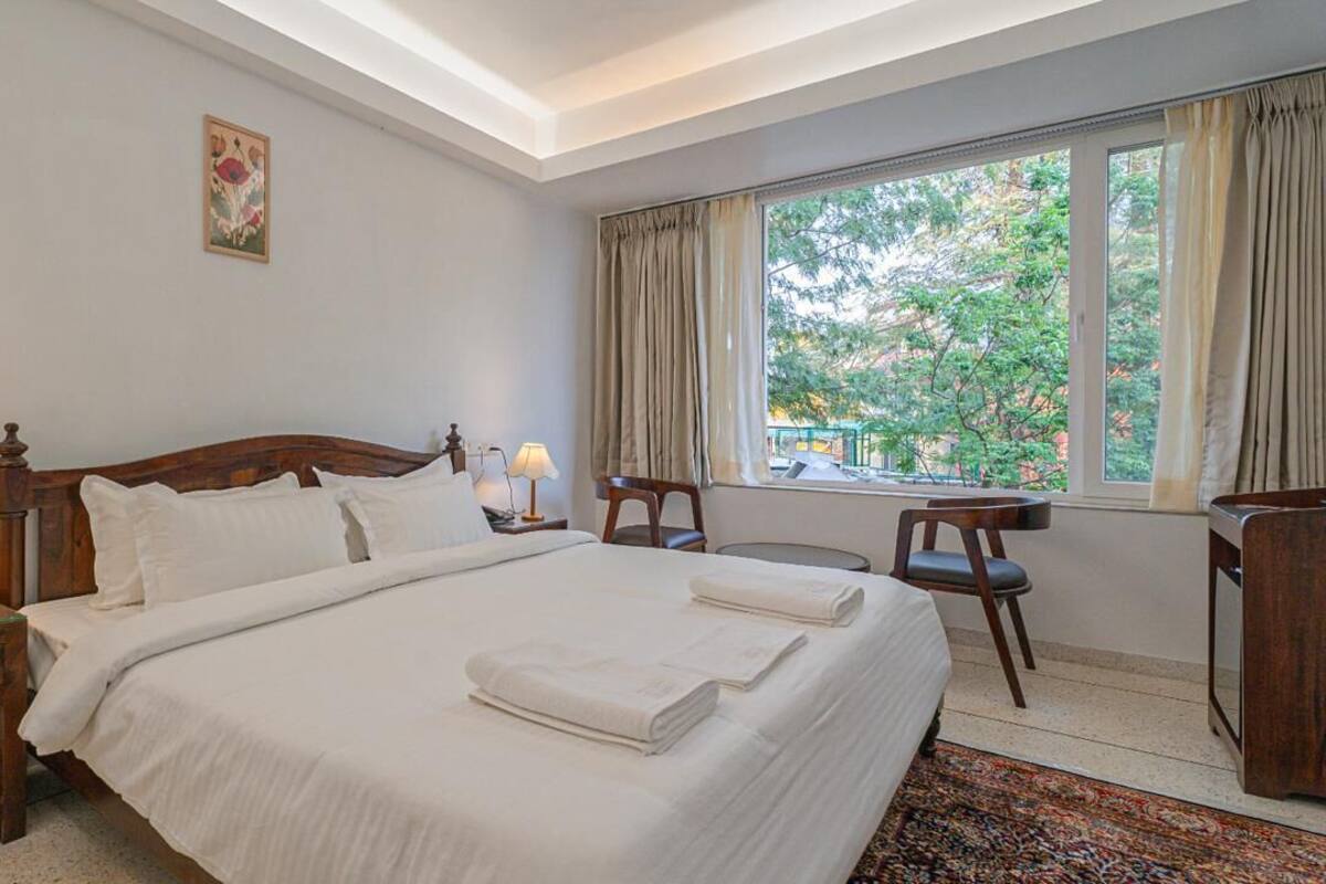 A hotel room with a large bed, a desk, a chair, and a window with curtains.