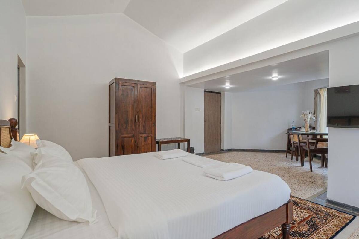 A hotel room with a bed, wooden wardrobe, desk, chair, and a television.