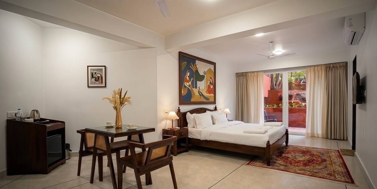A hotel room with a bed, a desk with a chair, a television, and a painting on the wall.