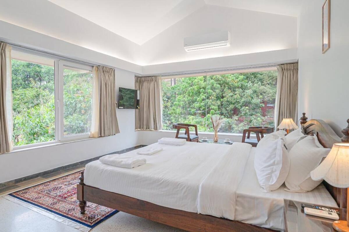 A bedroom with a large bed, a TV, and a view of greenery outside.
