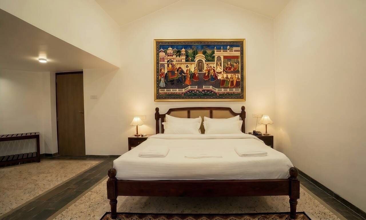 Habitación de hotel con una cama grande, dos lámparas de noche, un cuadro sobre la cama y una puerta a la izquierda.