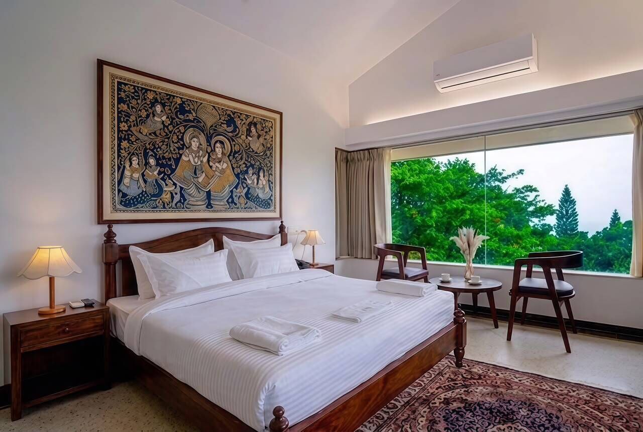 A hotel room with a large bed, a nightstand, a bedside table, a chair, a small table with a vase, and a large window with a view of trees.