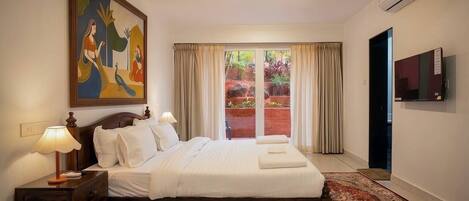 A hotel room with a bed, a nightstand, a lamp, a painting, a TV, and a view of a garden through a sliding door.