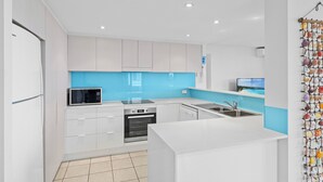 Een moderne keuken met witte kastjes, een blauwe achterwand, een magnetron, een oven en een spoelbak.