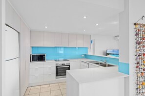 A modern kitchen with white cabinets, a blue backsplash, a microwave, an oven, and a sink. - Beach Days - Rooftop Jacuzzi with Ocean views - Sleep 8 people. (Marcoola)