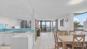 Een moderne keuken met een centraal eiland, een eetgedeelte met houten stoelen en uitzicht op de omgeving.