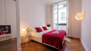 A hotel room with a bed, a bedside table with a lamp, a window with curtains, and a view of the outside balcony. - MARAIS, LIVELY, 3BR, REFURB., LIFT, 30–60 days ahead? Private offer FLO-VBp (Paris)