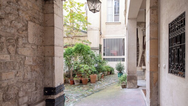 A narrow stone pathway leading to a courtyard with potted plants and a building with barred windows. - MARAIS, LIVELY, 3BR, REFURB., LIFT, 30–60 days ahead? Private offer FLO-VBp (Paris)