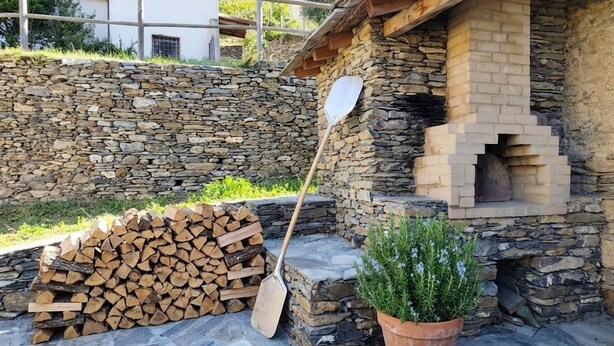 A stone building with a fireplace, a stack of firewood, and a shovel. - Casa Sud Miranda - rustico di paese (Borghetto d'Arroscia)