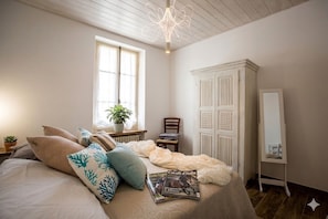 Ein Schlafzimmer mit einem Bett, einem Fenster, einer Zimmerpflanze, einem Stuhl, einem Kleiderschrank und einem Spiegel.