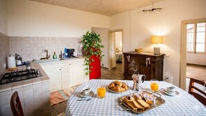 A kitchen with a gas stove, a sink, and a dining table set with breakfast. - Casa Sud Miranda - rustico di paese (Borghetto d'Arroscia)