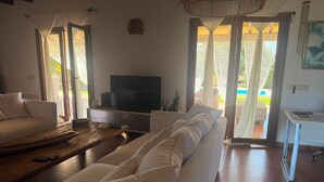 Una sala de estar con sofá, mesa de centro, televisor y vistas al exterior.