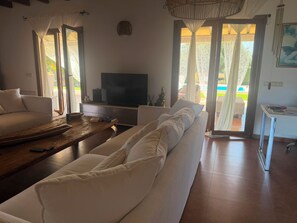 Ein Wohnzimmer mit einer Couch, einem Couchtisch, einem Fernseher und Blick ins Freie.