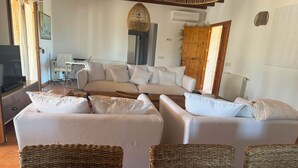 Amplia sala de estar con un conjunto de sofás, cestas de mimbre y una lámpara colgante.