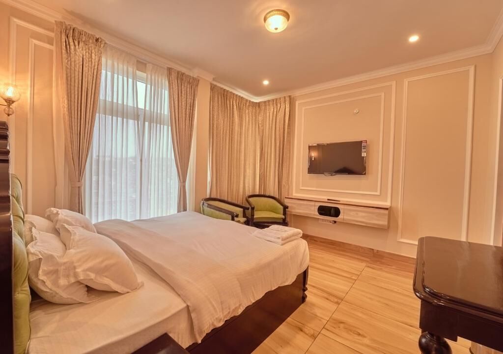A hotel room with a bed, a TV mounted on the wall, a chair, and a wooden floor.