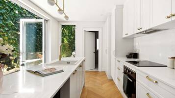 A modern kitchen with white cabinetry, a wooden herringbone floor, and a window with a view of greenery.