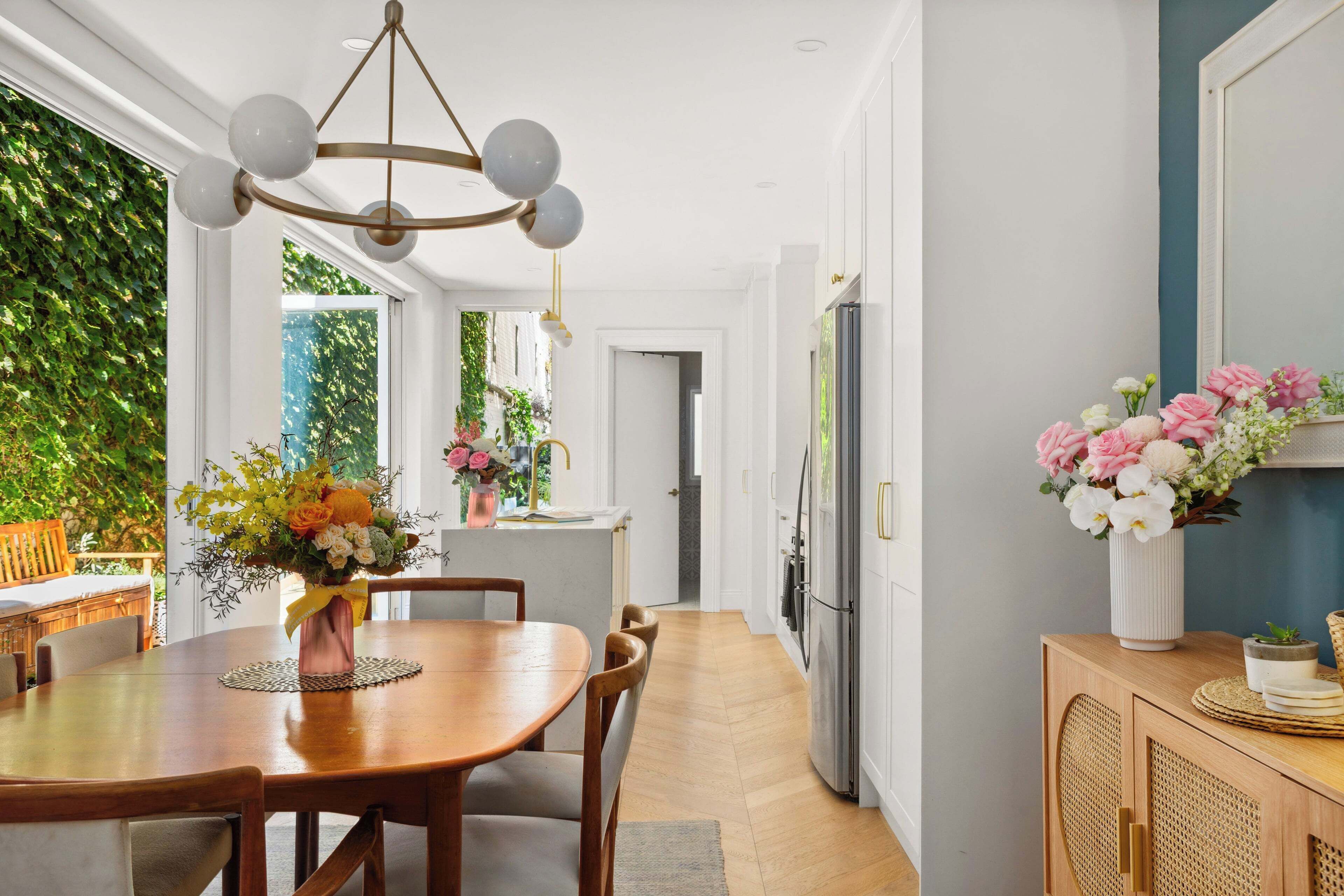 A modern kitchen with a dining area, a chandelier, and a view of greenery outside.
