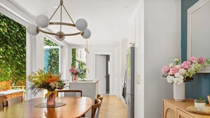 A modern kitchen with a dining area, a chandelier, and a view of greenery outside. - Chic Inner-City Oasis in the Heart of Sydney (Redfern)