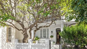 A white building with a large tree in front, a gate, and a number '75' on the wall. - Chic Inner-City Oasis in the Heart of Sydney (Redfern)
