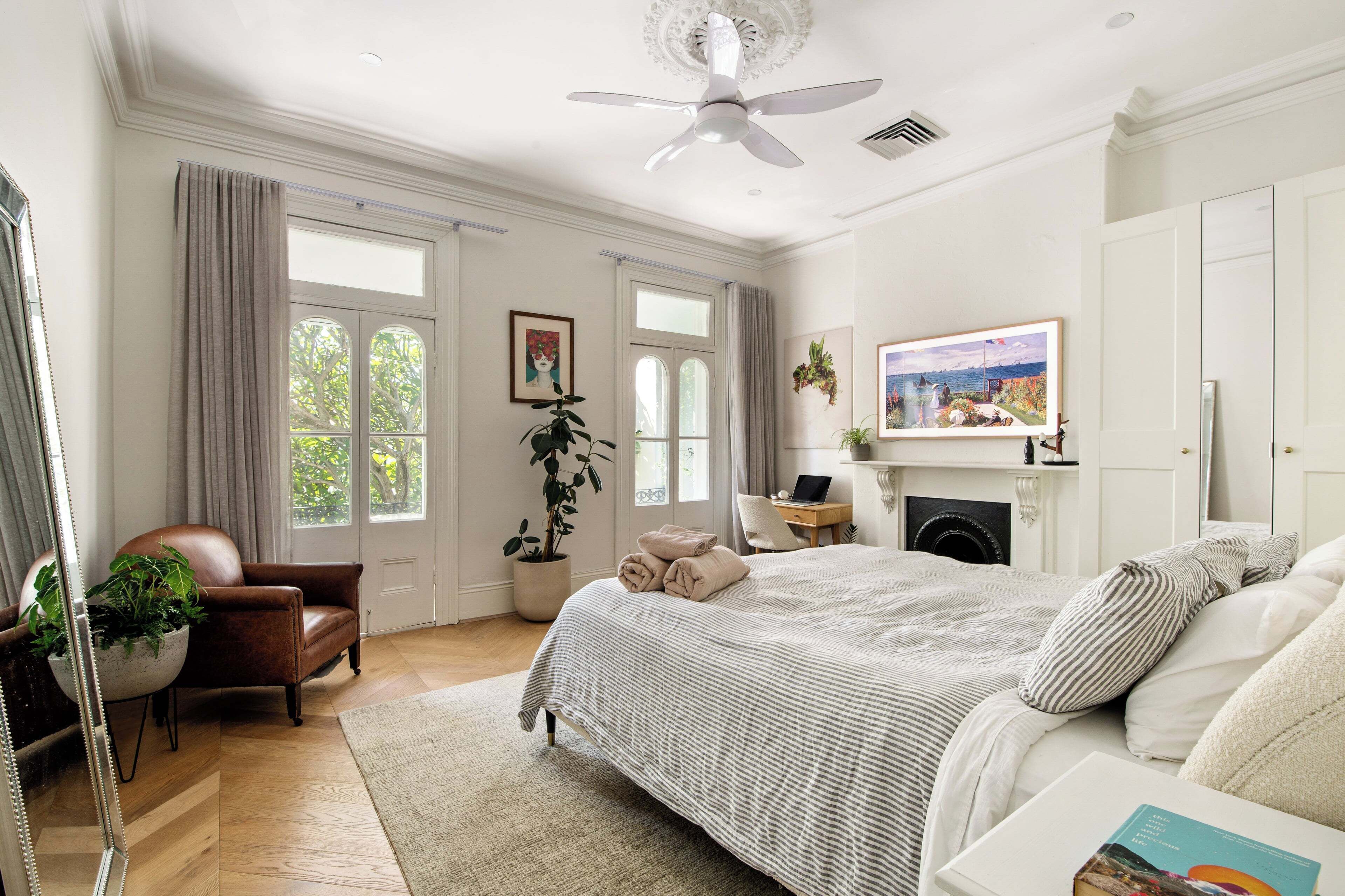 A well-lit bedroom with a large bed, a desk, a chair, and a fireplace.