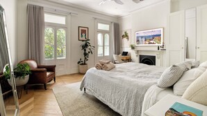 A well-lit bedroom with a large bed, a desk, a chair, and a fireplace. - Chic Inner-City Oasis in the Heart of Sydney (Redfern)