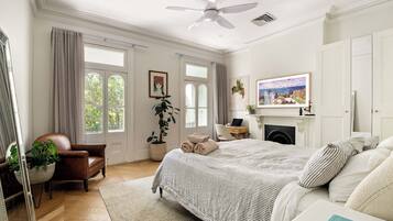 A well-lit bedroom with a large bed, a desk, a chair, and a fireplace.