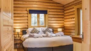 Ein Schlafzimmer in einer Blockhütte mit einem Bett, Nachttischlampen, einem Fenster und einem Holzboden.