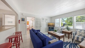 A modern living room with a blue sofa, red bar stools, a wooden coffee table, and a TV. - Walk to Lido Beach, Restaurants, Kayaking & Pool (Sarasota)