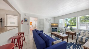 Ein modernes Wohnzimmer mit einem blauen Sofa, roten Barhocker, einem Holztisch und einem Fernseher.