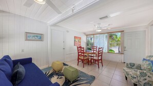 A room with a blue sofa, a dining table with red chairs, a wicker ottoman, and a window with blinds. - Walk to Lido Beach, Restaurants, Kayaking & Pool (Sarasota)