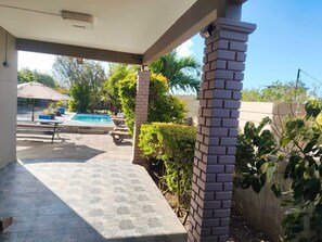Eine überdachte Terrasse mit Pool, Gartenmöbeln und viel Grün.