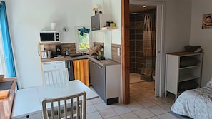 Une petite cuisine équipée d’un four à micro-ondes, d’une machine à café et d’un évier. Un coin repas avec une table et des chaises est à disposition, ainsi qu’une cabine de douche avec un rideau à motifs.
