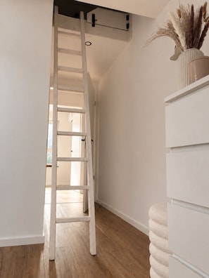 Ein Flur mit einer weißen Leiter, einer weißen Wand und einem weißen Schrank mit einer Vase getrockneter Pflanzen.