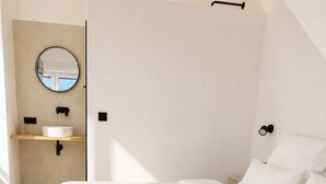 Une chambre à coucher avec un lit, une table de chevet, un miroir rond et une petite fenêtre.