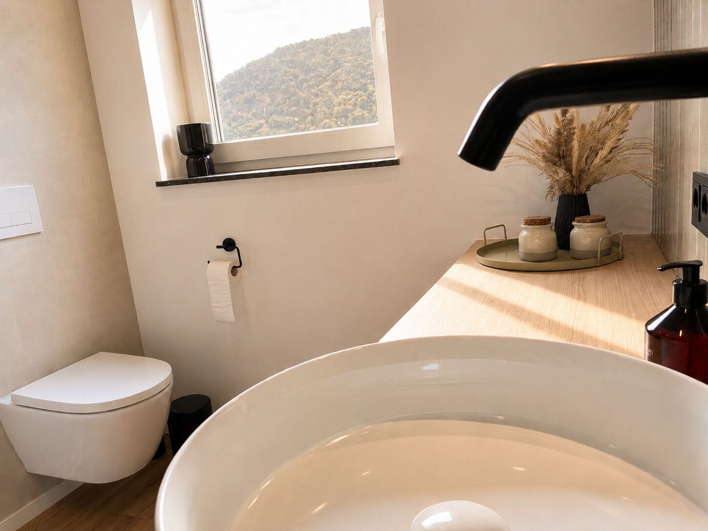 A bathroom with a toilet, sink, window, and a shelf with jars.