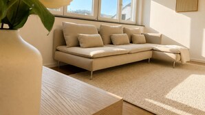 Un salon moderne avec un canapé d’angle beige, une table basse en bois et une grande fenêtre donnant sur le ciel.