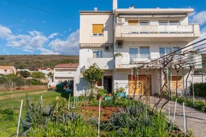 Ein zweistöckiges Wohnhaus mit Balkon, einem Garten mit verschiedenen Pflanzen und blauem Himmel.