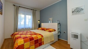 Ein Schlafzimmer mit einem Bett, einem Fenster mit Vorhängen, einem Nachttisch, einer Lampe und einer Klimaanlage.