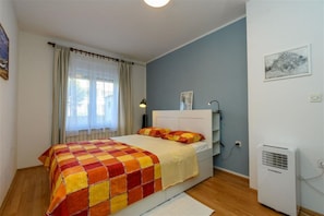Ein Schlafzimmer mit einem Bett, einem Fenster mit Vorhängen, einem Nachttisch, einer Lampe und einer Klimaanlage.