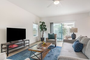 A living room with a TV, coffee table, sofa, and a plant.