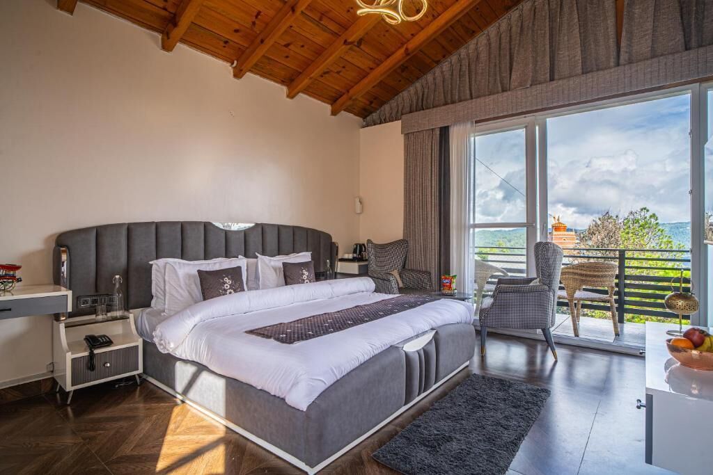 A bedroom with a large bed, a nightstand, a chair, and a view of the outdoors.