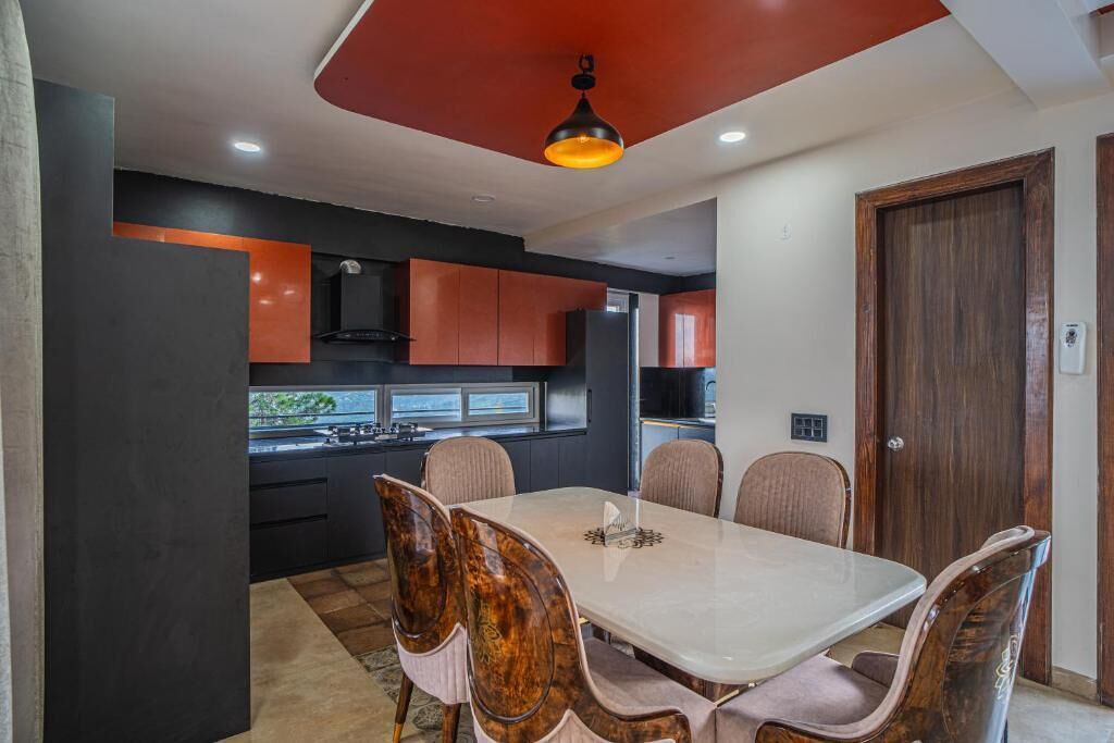 Un espace de salle à manger moderne avec une table et des chaises blanches, une cuisine en arrière-plan et une porte en bois.