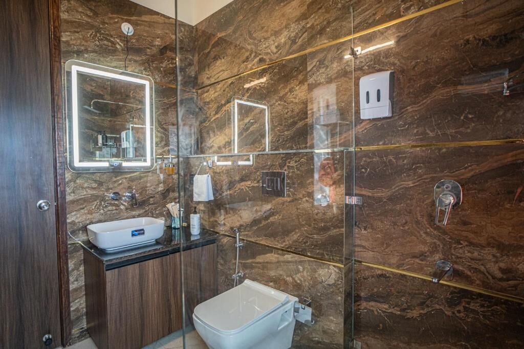A modern bathroom with a marble wall, a glass shower enclosure, a white sink, and a mirror with built-in lighting.
