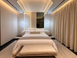 Une chambre d’hôtel moderne avec un grand lit, un banc et une vue sur le paysage urbain par la fenêtre.