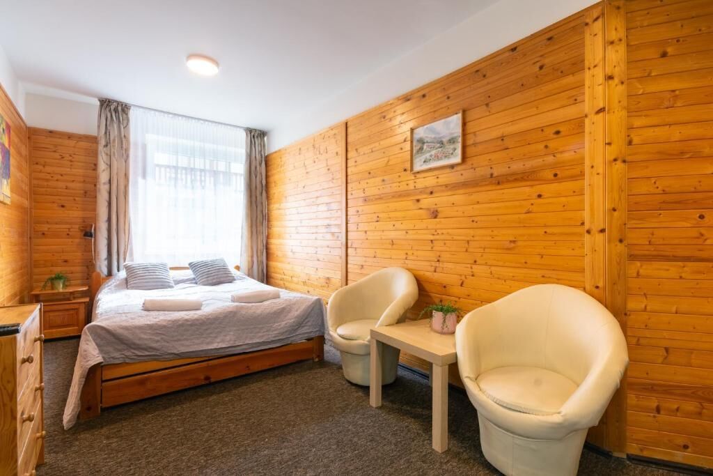 A bedroom with a bed, two chairs, a small table, and a window with curtains.